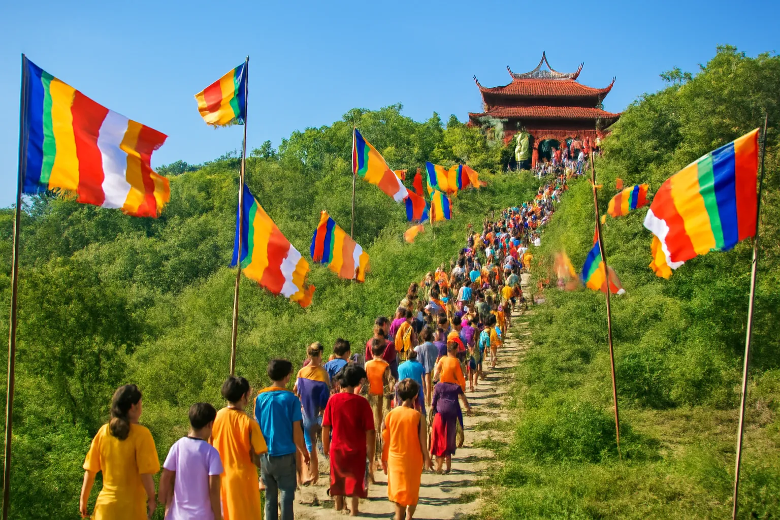 Dòng người áo sáng màu đi trên lối lên chùa, cờ ngũ sắc bay phía trên